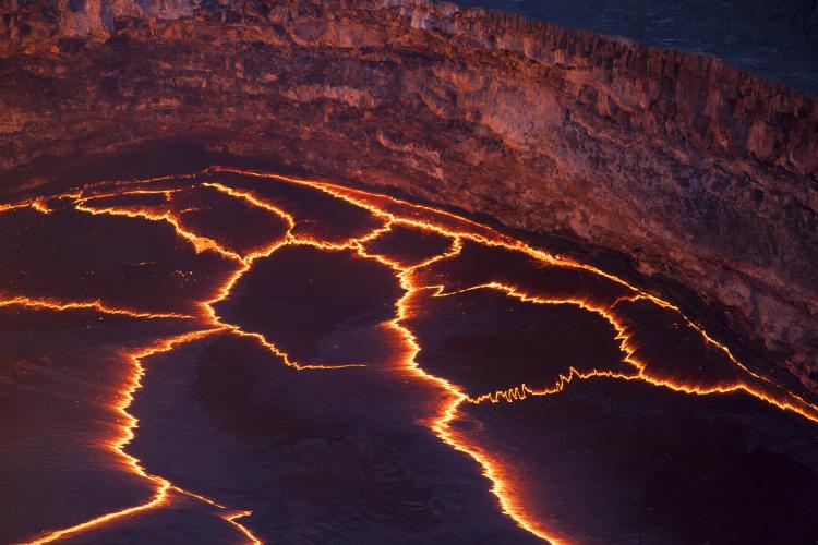 Incandescent lines mark the boundaries between migrating crustal plates on the surface of the lava lake in HALEMAUMAU crater.  Here, and at other lava lakes across the world, these rifting zones have a characteristic zigzag pattern.  