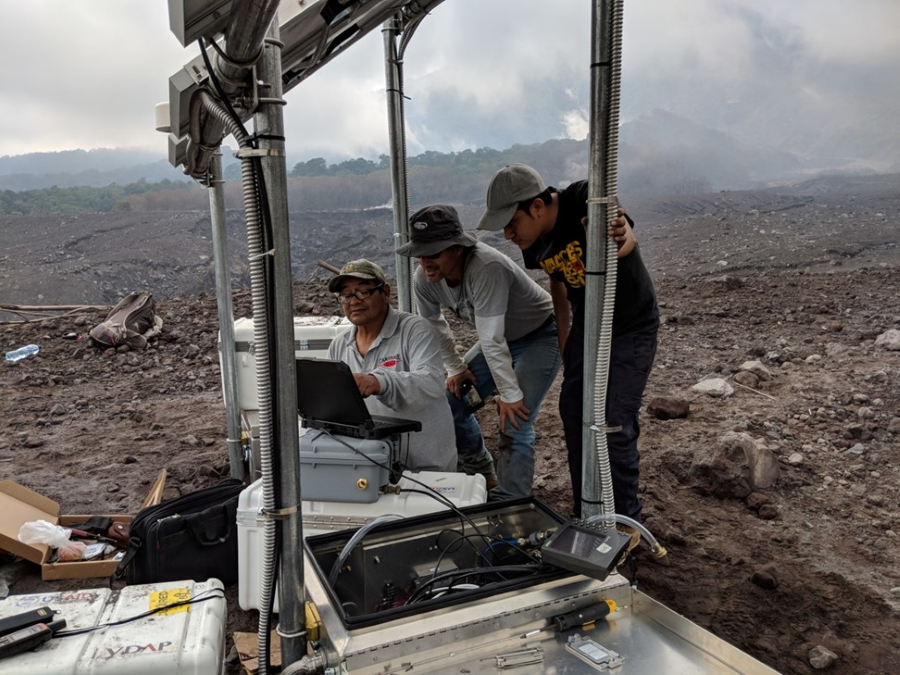 Volcano scientists from INSIVUMEH check instrumentation at a newly-installed seismic and infrasound monitoring station at Fuego volcano, Guatemala, in 2018. USGS image.  (Click image to view full size.)